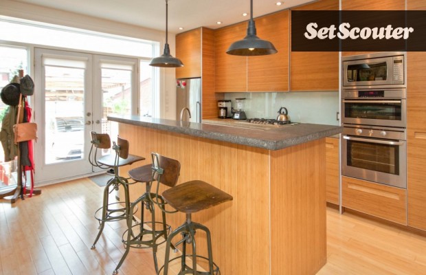 This kitchen is cool and contemporary with unique wood-panelled cabinetry. Monica's multi-level island has a sink and acts a a breakfast bar. The wall of windows allows the kitchen to be filled with natural light, ideal for shooting.