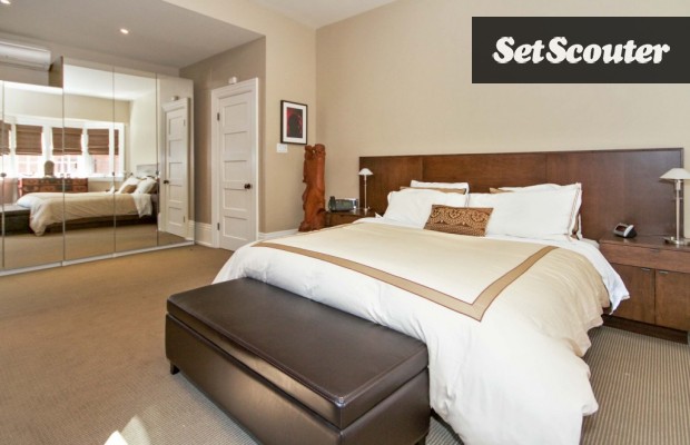 This master bedroom is a spacious, refined classic. The dark wood headboard beautifully offsets the naked walls, a stylish design that will never go out of style. Tim's bedroom is flooded with natural light, and features dazzling floor-to-ceiling mirrors.