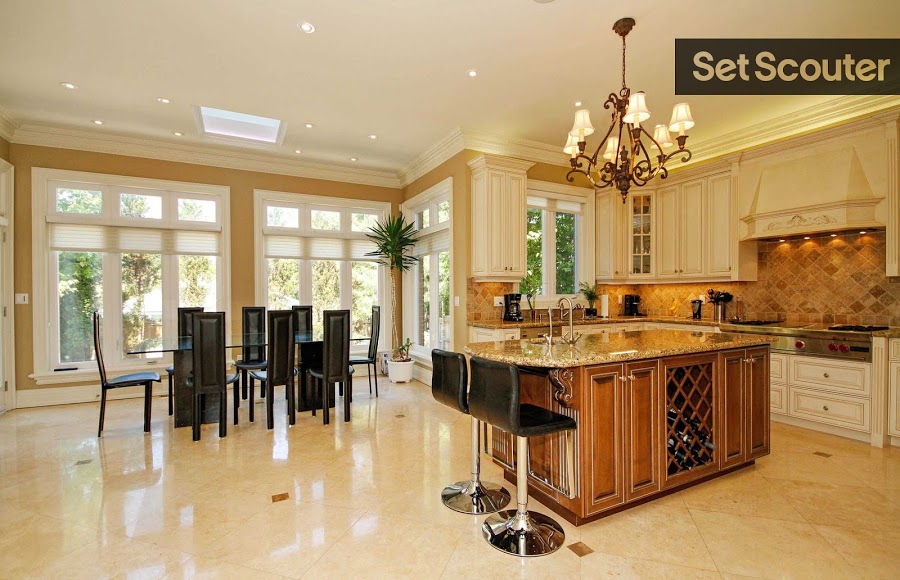 A kitchen with wall-to-wall windows and earth tones is both warm and inviting. Minimalist furniture like the sleek black dining chairs and leather bar stools add an edgy touch to the classic design of Esti's cupboards, kitchen island and granite counter tops.