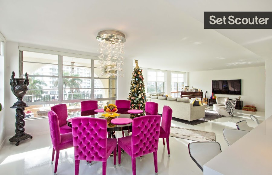 An open concept plan means enough room for both a living and dining area. Large windows mean ample natural light, allowing indoor fixtures to feel cool and interesting. Hot pink chairs surround a sleek dining table and are a fun statement piece in a clean white room.