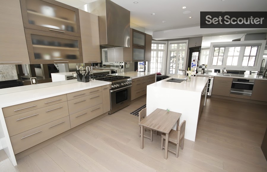 A taupe kitchen with stainless steel appliances looks modern and inviting. Neutral cupboards complement the beige hardwood floors and quaint center island. An open concept with natural light from the living room brightens, while a kids breakfast table adds character to the space.