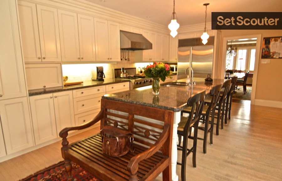 A 12-foot granite island looks modern and sleek accompanied by wooden bar chairs. New appliances dressed in metallic, offset the traditional white cupboards and hardwood floors, keeping this kitchen looking classic but trendy.