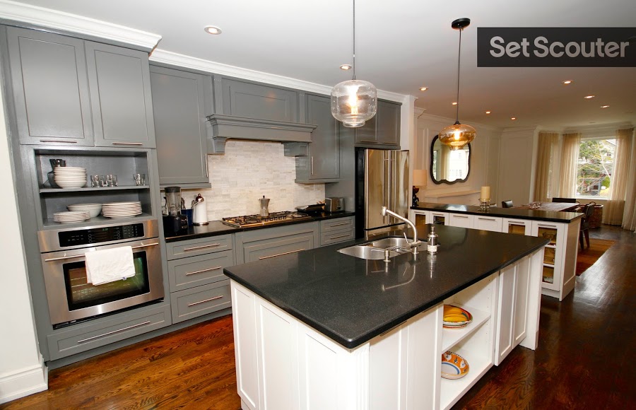 This modern home showcases an exposed kitchen with gourmet appliances and a large island with an embedded sink. Light grey cupboards compliment the rustic undertones of the dark hardwood floors and open shelving make this space cozy and inviting.