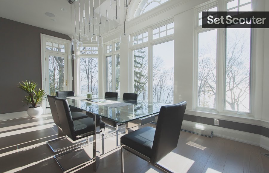 Crisp white trimming contrasts charcoal grey in this minimalist dining area. Floor-to-ceiling windows allow natural light to illuminate the room while providing a magnificent, scenic view outdoors. A glass table below an array of pendant lighting is a stylish addition to a clean setup.