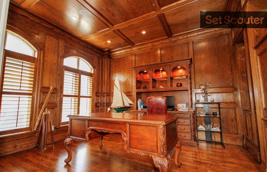 A solid wood study is charming with engraved ceilings and covert lighting. Arched windows add style while allowing natural light to brighten the room. In the middle of the room, a large antique desk with a red leather chair are the perfect statement pieces.