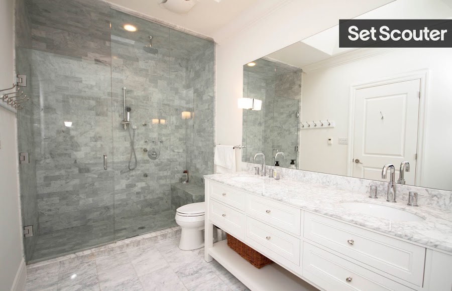 This stylish bathroom is chic with its marble counters and flooring to match. A step in shower featuring full-length glass doors looks both sexy and sophisticated, while white walls and silver fixtures keep the area bright and clean.