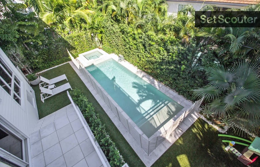 Behind the home, a wall of greenery hides an underground pool. Marble tiles and white lounge chairs give this area an upscale and exclusive look. Between the privacy and sleek décor this area could be filmed as a country club amenity.