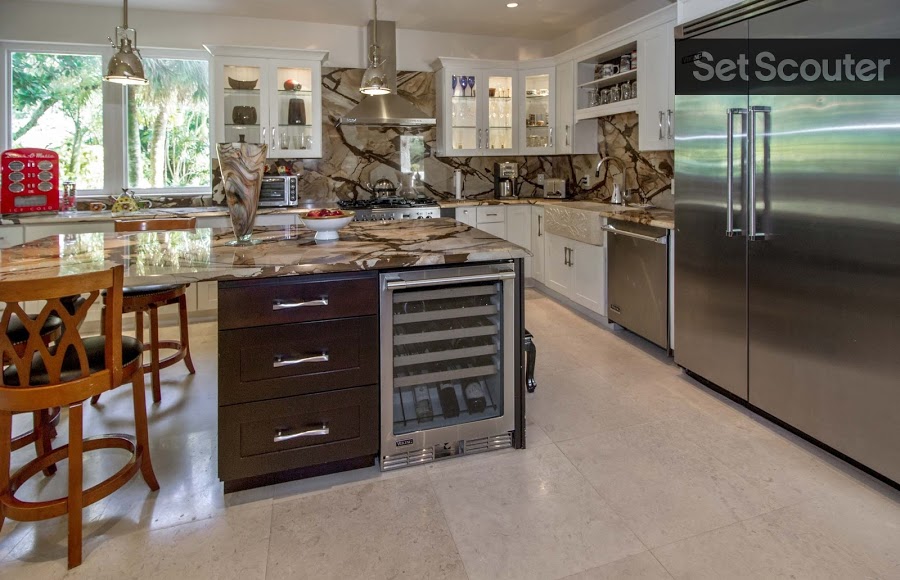 Vanessa’s kitchen is surely one-of-a-kind in its textures and design. Mounted cabinets with white trim are a simple complement to the swirled marble countertops and backsplash. The kitchen island is complete with a seating area and a wine cooler, while touches of stainless steel tie this spacious area together.
