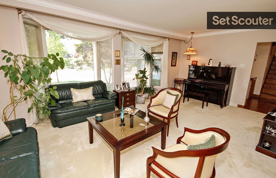 The living room is decorated in deep green and white with hints of wood to match the rest of the home. A stained-glass lamp hangs over an upright piano complimenting the rich, warm tones and style throughout the space. A touch of greenery and soft, white curtain leave the space light and airy.