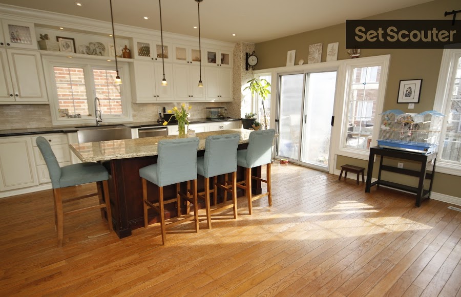 Noami's warmly lit kitchen is large and inviting. Hard wood floors compliment the cool tones in her bar stools and granite counter-top, while contrasting elegantly with the dark wood of the kitchen island. White cupboards and touches of greenery keep this space bright and fresh.
