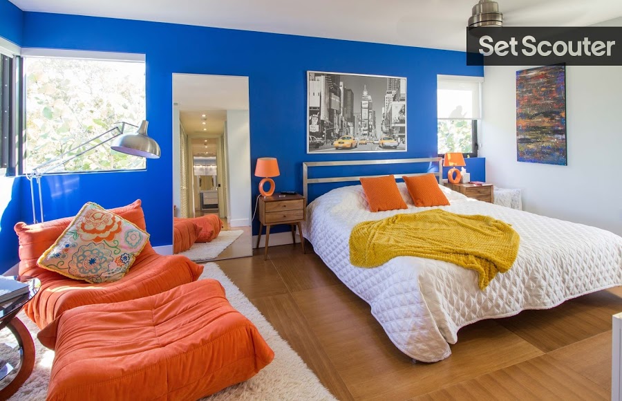 Opposites attract in this sharp-dressed, blue and orange master bedroom. Filled with character and a modern take on retro decor, Tony's livens his bedroom with complimentary colours and softens it with white bedding and minimalist furniture. A tall, standing mirror gives the illusion of field while wooden flooring and side tables leave the room modern and fresh.