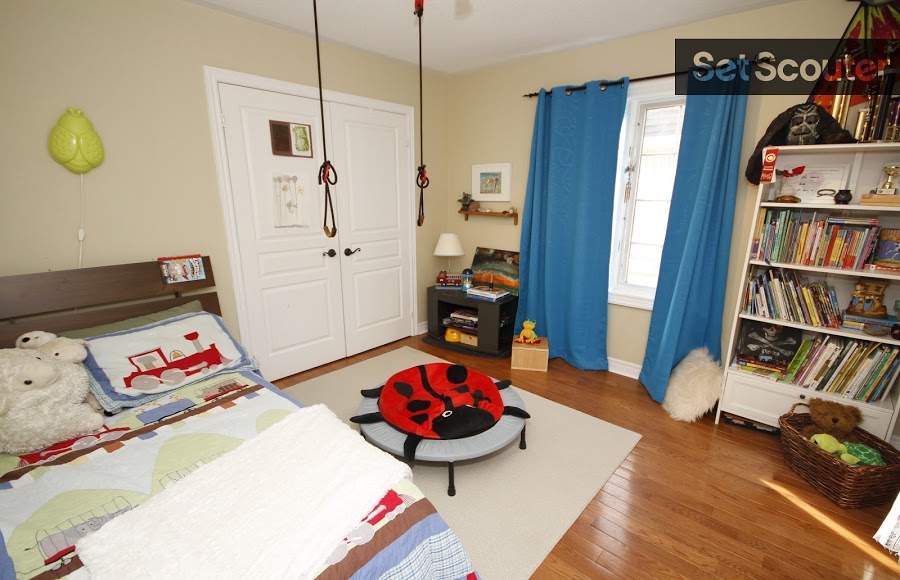 Upstairs, a large kid's bedroom is adorned with youthful design. Books littler the shelves and a variety of toys are spread around the room. This room is playful and modest, with low-hanging ropes, a trampoline along with it's adorable lady-bug cover.