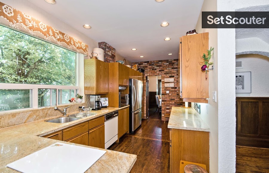 Rhonda's warm wood kitchen is bright and flooded with diverse textures and patterns. An exposed brick accent wall combined with hardwood floors and orange, paisley wallpaper give this charming kitchen a dash of rustic personality. With a large window and beige, marble counters, this kitchen comes together to create a refreshing and delightful space.