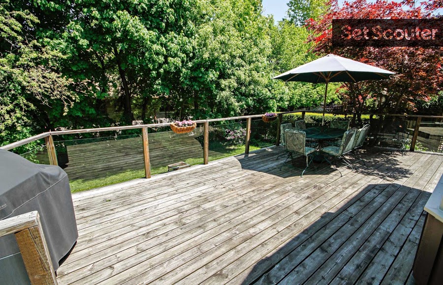 A large, elevated, wooden deck with a sheltered seating area is perfect for the warm Canadian summers. Surrounded by large, old trees and potted flowers, this classic backyard patio is spacious and inviting.