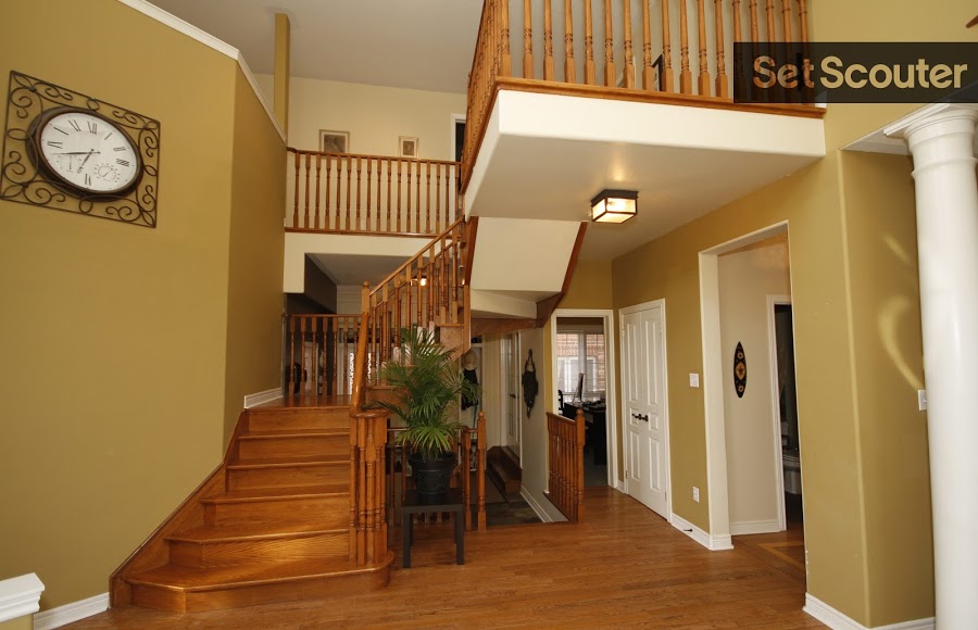 The entryway way to this family home is traditional and modern design, with a classic wooden staircase, gold walls and sharp, white accents. Simplicity in decor keeps this space open and welcoming, and the interior balcony is both charming and functional for overhead shot.