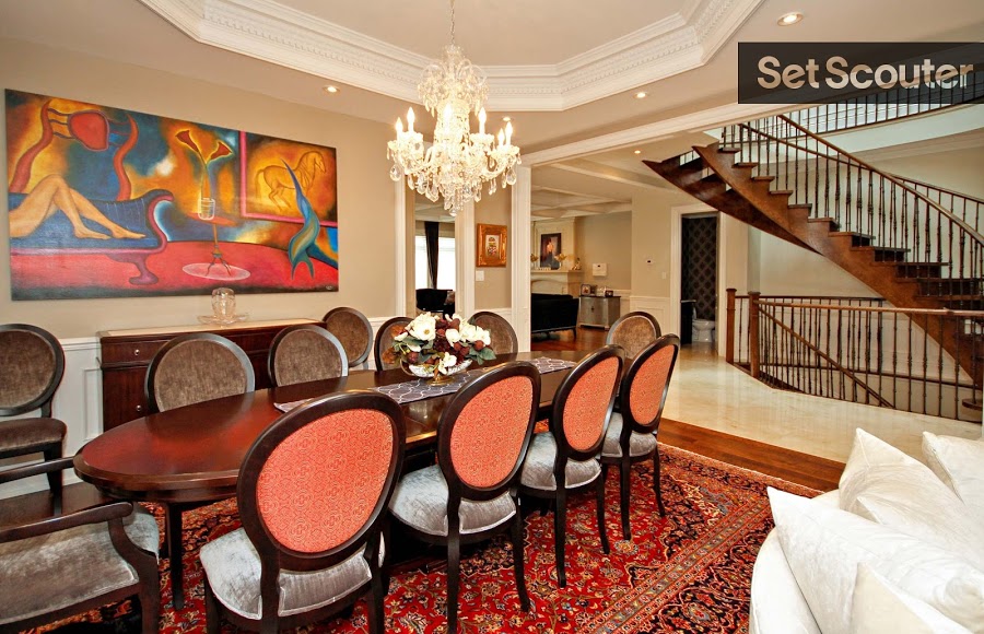 This dining area is rich and full of character. Warm tones of red and orange are consistent throughout the space, from the beautiful, detailed carpet, to the contemporary art-work. Michael's deep, brown-red dining table and chairs make a great statement piece along with a bright, crystal chandelier hanging above.