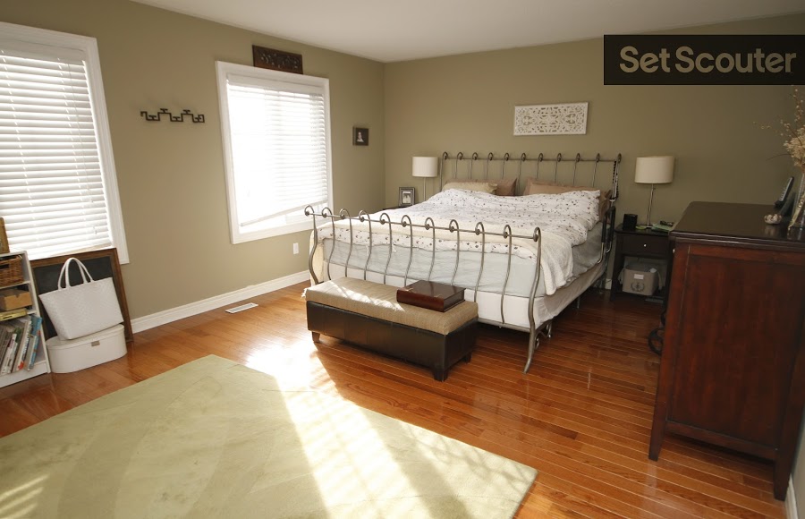 Upstairs sits a bedroom large in space but quaint in ambiance. A taupe carpet covers classic hardwood floors while sunlight pours in from two large windows. Delicate silver bed rails compliment the rich tones and small embellishments throughout the space.