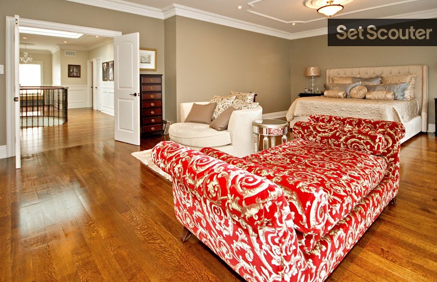 The décor in this spacious, master bedroom brings in many of the classic elements seen throughout the home. This massive room is anchored by warm, neutral tones, while a red and gold, velvet chaise ties together a luxurious seating area at the end of the bed.