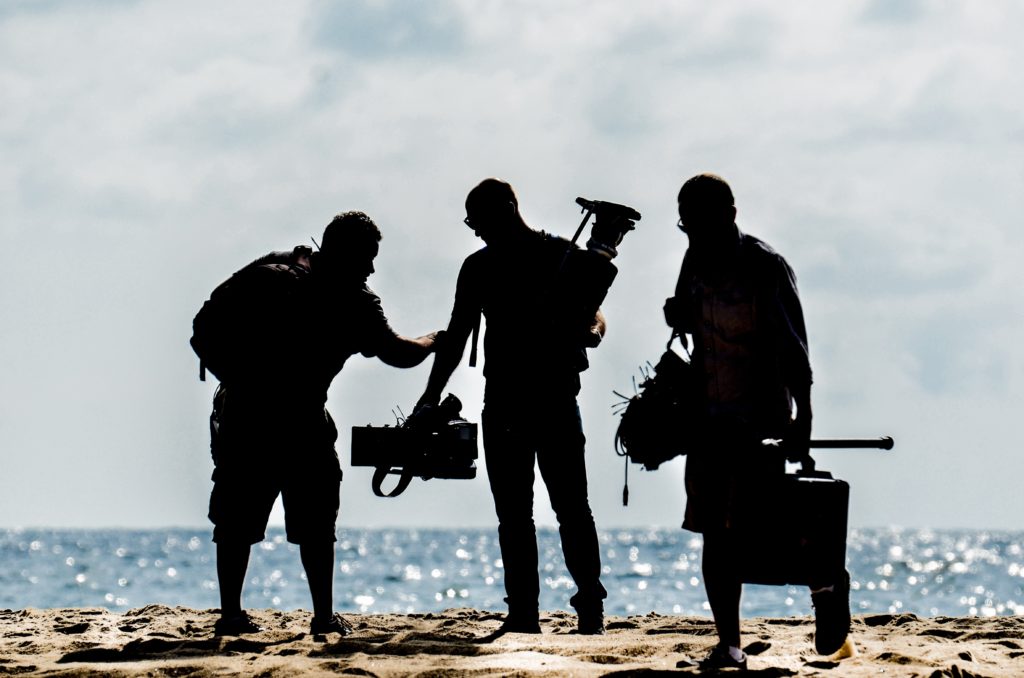 Who's your go-to crew? Your team can be a big help in caring for your mental health on a film set. Pictured: the silhouette of three men holding camera gear at the beach.
